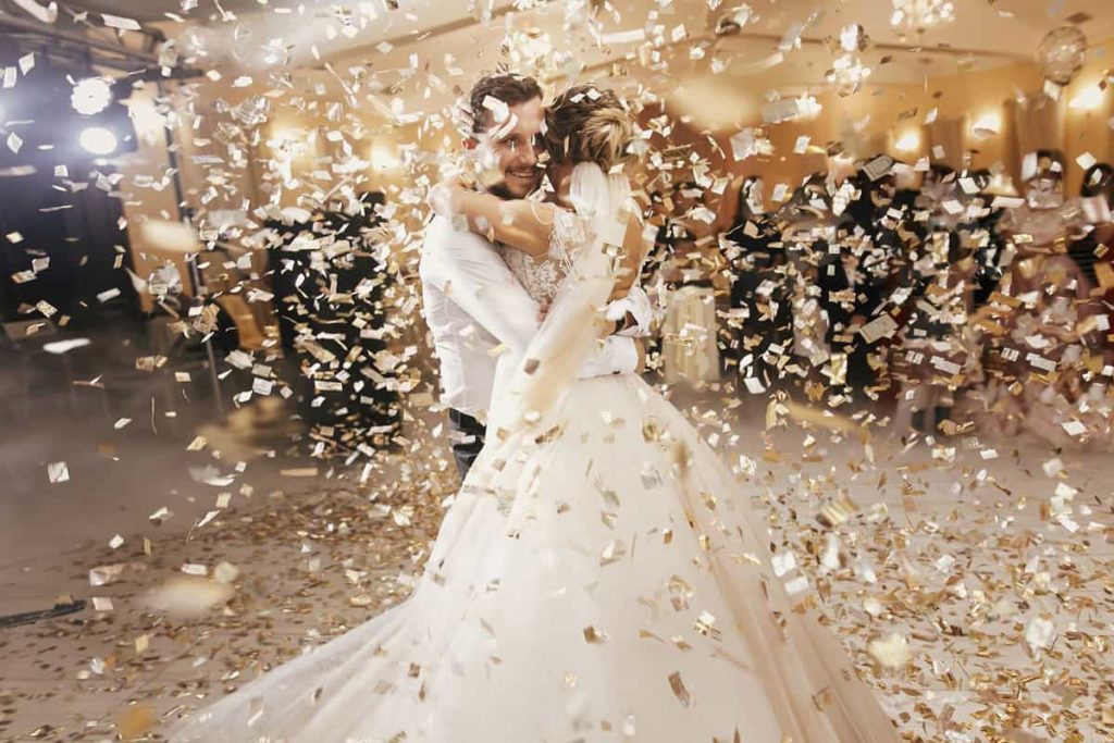 La novia y el novio recién casados ​​bailan en medio de una lluvia de confeti plateado y dorado en la recepción de su boda.