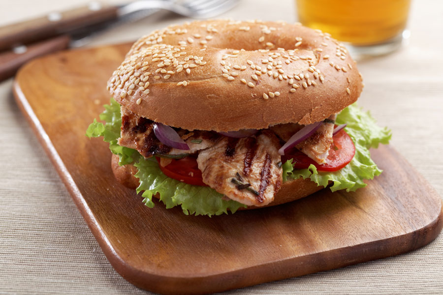 Grilled chicken sandwich with lettuce, tomatoes, and red onions on a sesame seed bun.