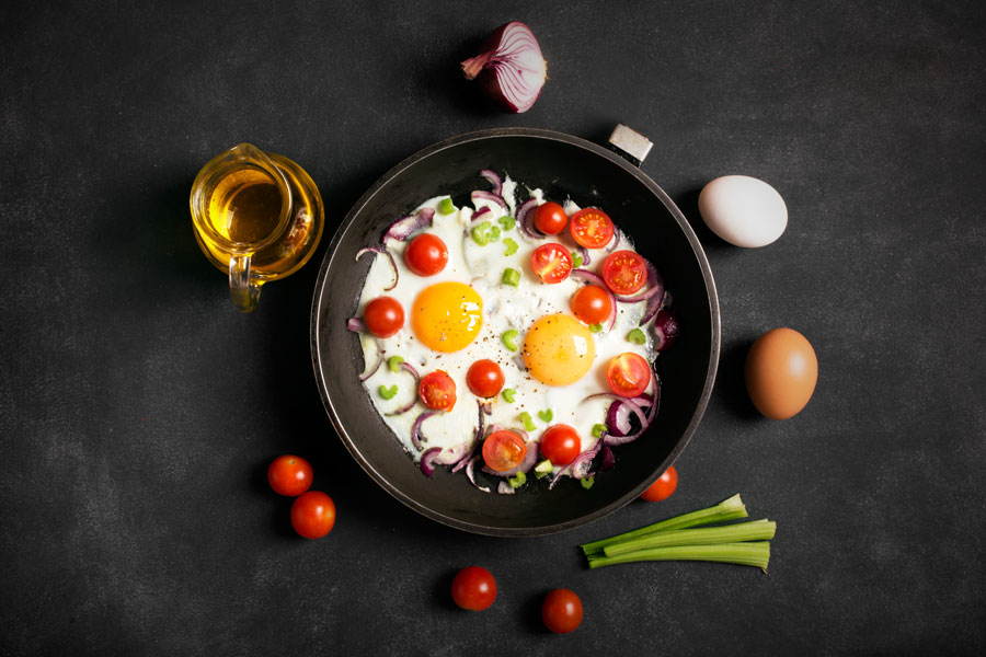 Eggs frying in a skillet with sliced cherry tomatoes, red onions, and leeks.