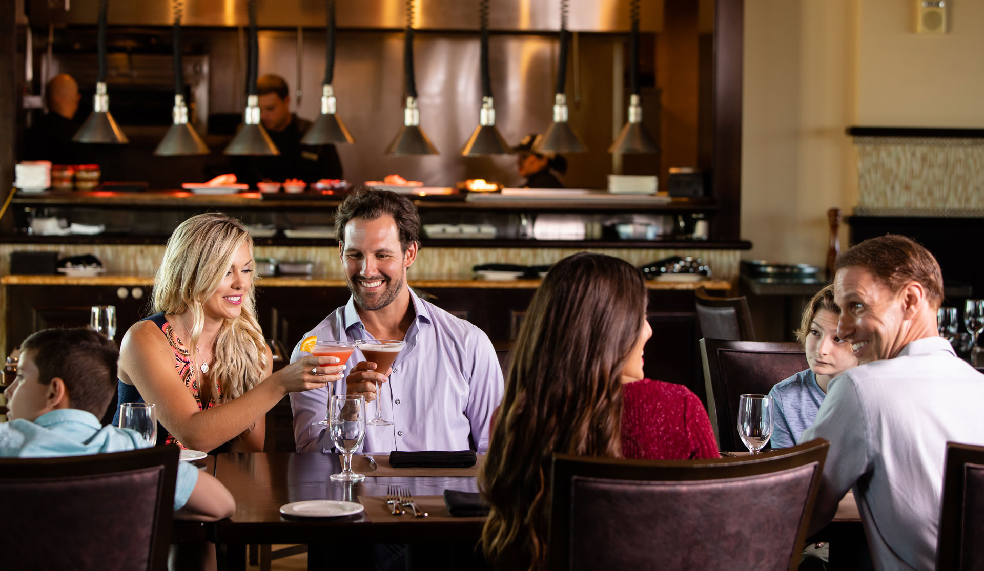 Couple toasts with Martini glasses while sitting with family at Traditions restaurant.