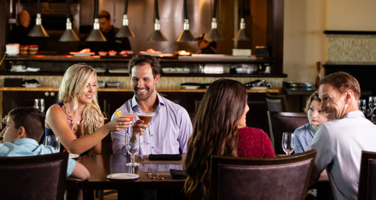 Couple toasts with Martini glasses while sitting with family at Traditions restaurant.