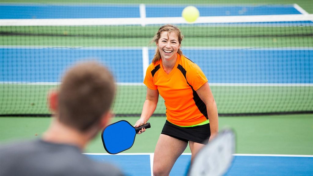 Couple playing pickle ball on a clay tennis court.