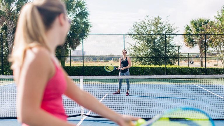 Two women playing tennis on a clay court at Reunion Resort.
