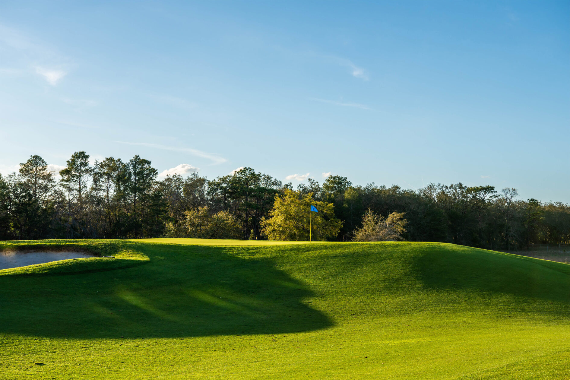 Golf course at The Bear’s Den Resort Orlando with hills, sand traps, and a single flag marking the hole on a distant putting green.