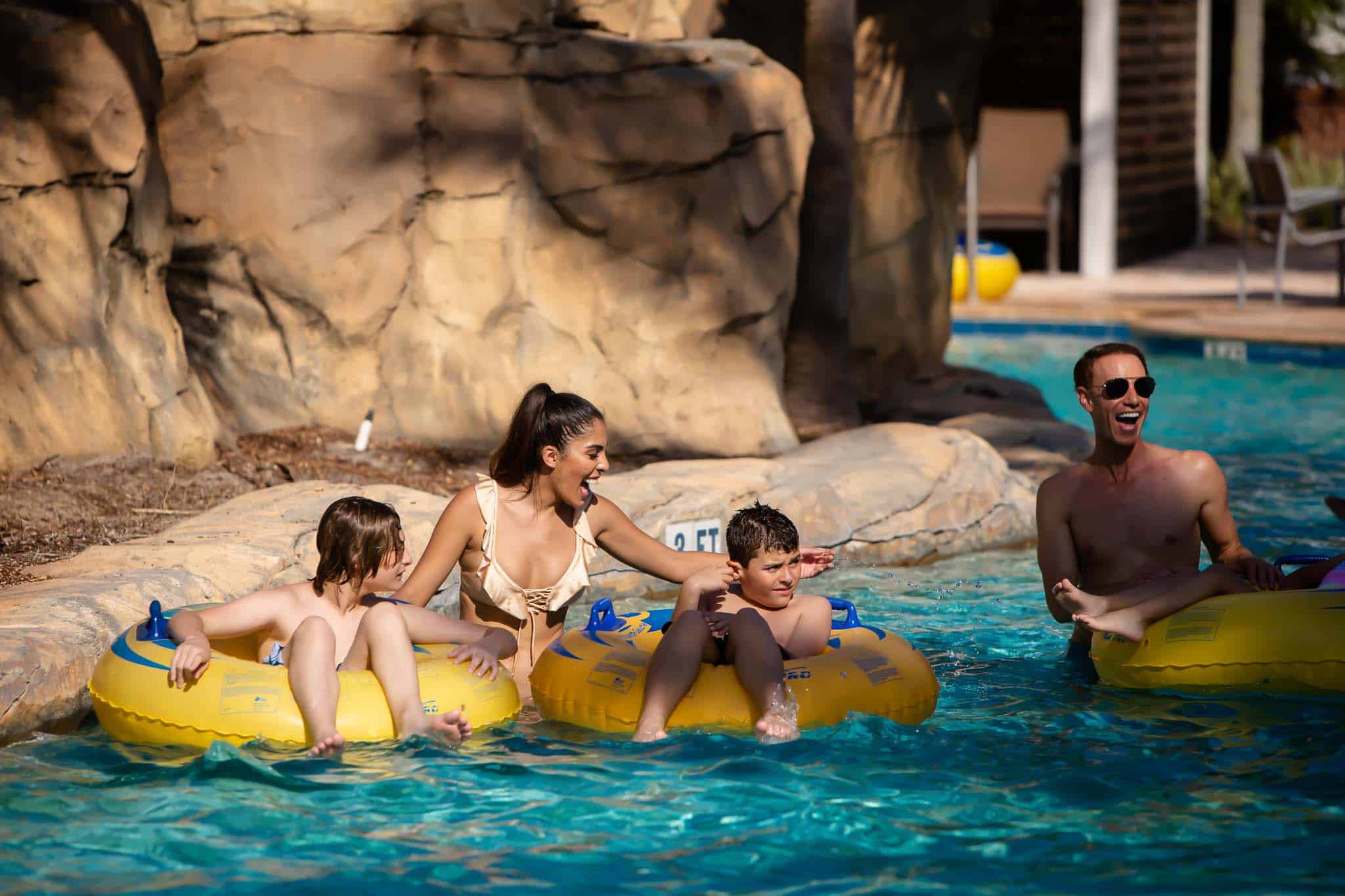Happy mom and dad push their kids riding in tube floats in the lazy river at The Bear’s Den Resort Orlando’s water park.