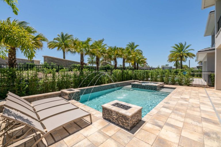 Private pool with fire pits, fountain, and hot tub in a backyard lined with palm trees.