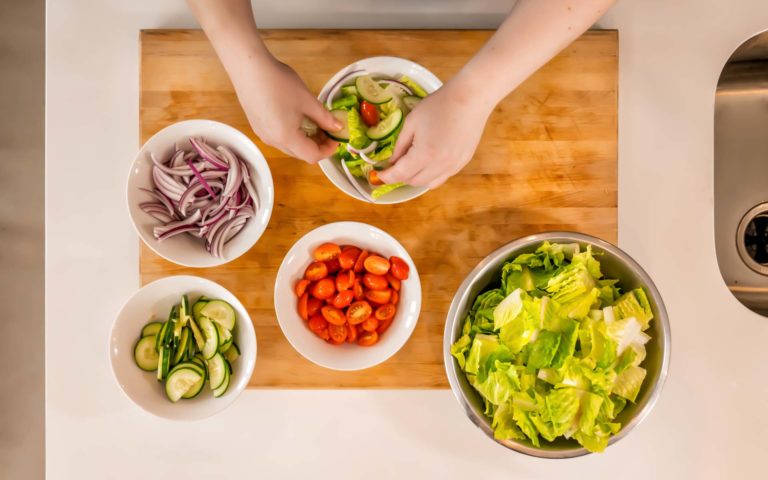 Hands putting salad ingredients into a bowl.