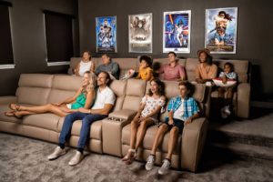 Large family of grandparents, parents, and kids happily watching a movie in a Bear’s Den Resort Orlando theater room.