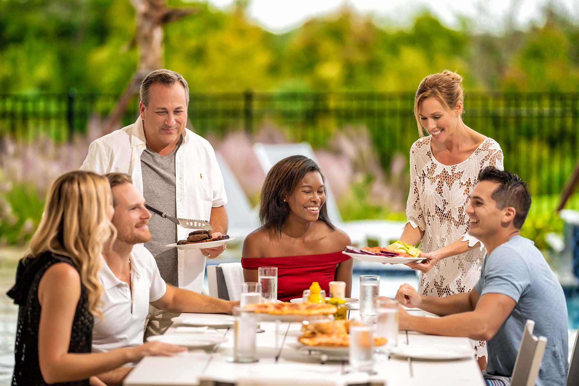Group of adults gathered around a table of grilled food in the outdoor summer kitchen lanai of a Bear’s Den resort residence.