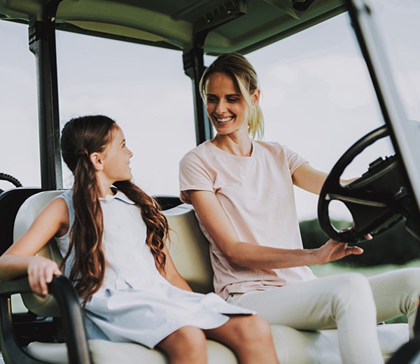 Mother and daughter riding on a golf cart.