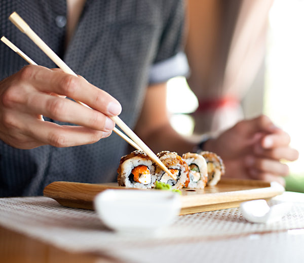 Hands picking up sushi with chopsticks.