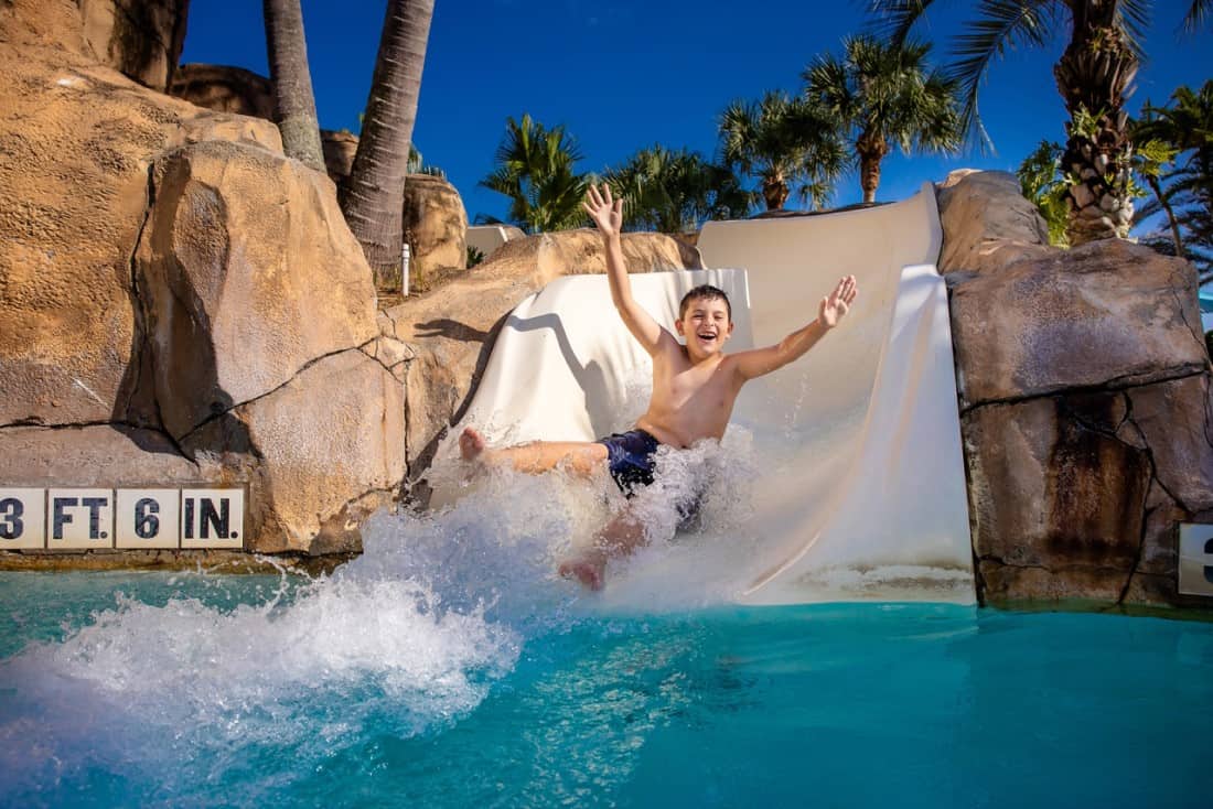 Young boy smiles while riding a water slide.