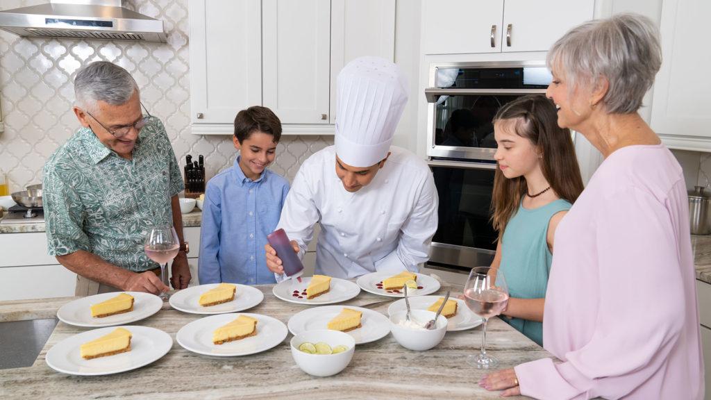 Chef decorating cheesecake dessert plates with sauce in front of family