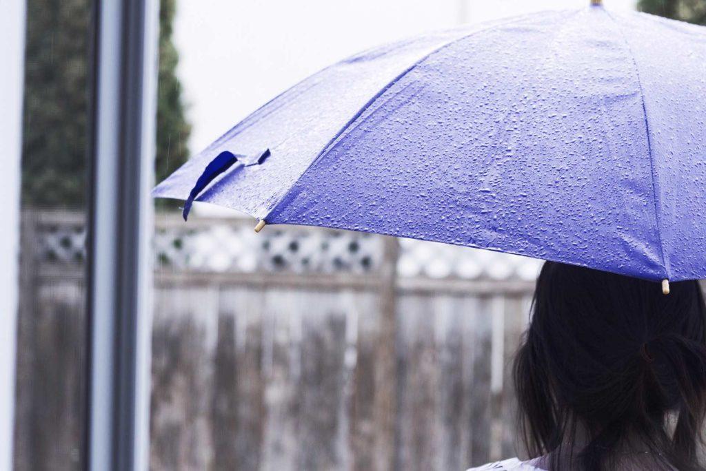Girl standing under purple umbrella in the rain