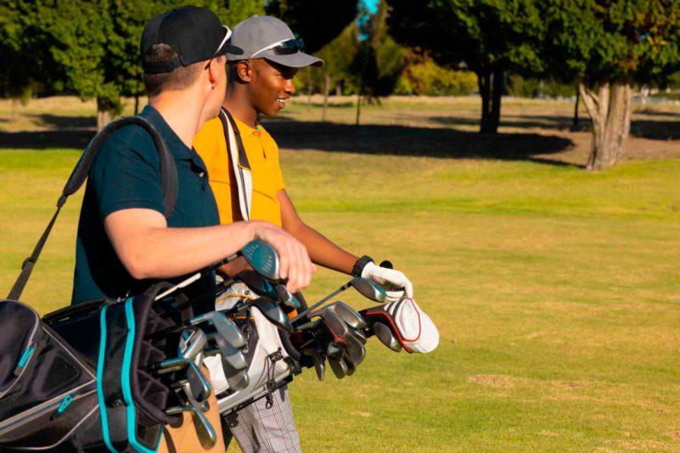 Two male friends carrying golf clubs on a green