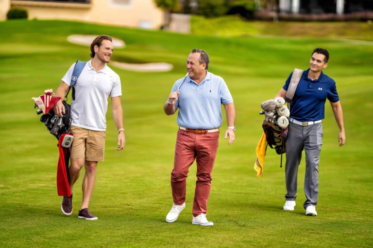 Grupo de tres hombres caminando con equipos de golf en los campos exclusivos de Bear's Den Resort Orlando.