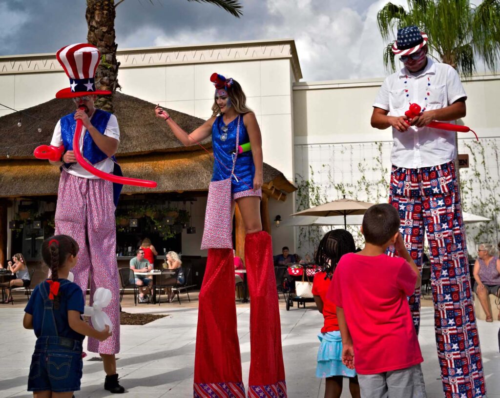 Street performers on stilts wearing USA themed attire making balloon animals at the Promenade at Sunset Walk