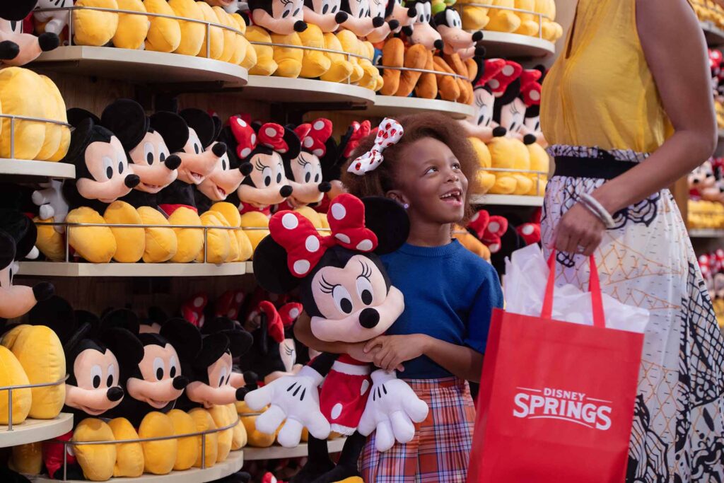 Young girl shopping for a Minnie Mouse stuffed animal with her mom in Disney Springs